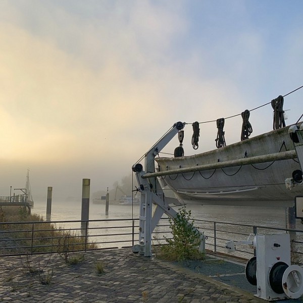 Nebelverhangene Flussmündung an der Lesum mit hochgezogenem Boot.