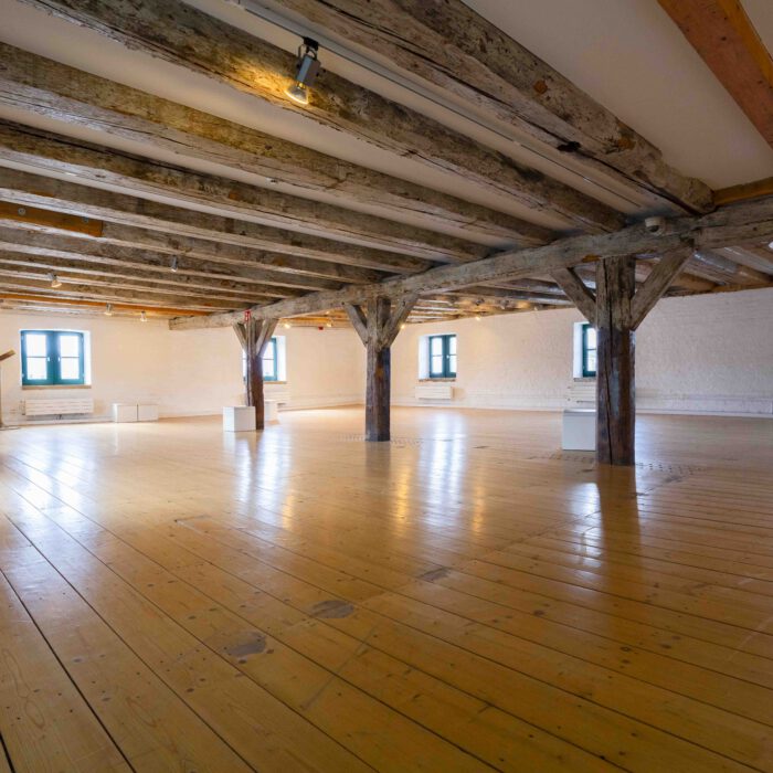 Weitläufige Galerie-Etage im Vegesacker Geschichtenhaus mit sichtbaren Holzdeckenbalken und hellem Holzdielenboden, vorbereitet für wechselnde Ausstellungen.